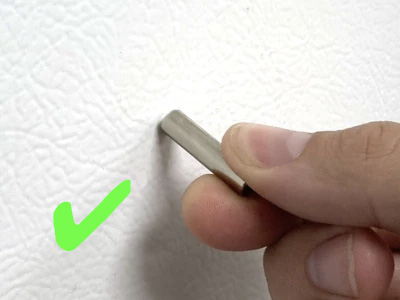 Hand easily removing neodymium cylinder magnet from fridge