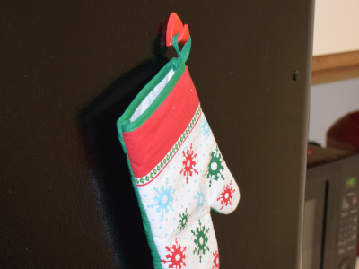 Plastic hook magnet holding holiday oven mitt on a black fridge