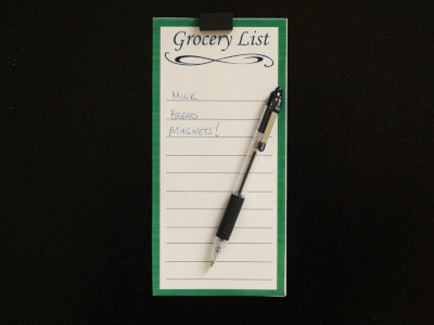 Magnets holding a pen and grocery list to a refrigerator